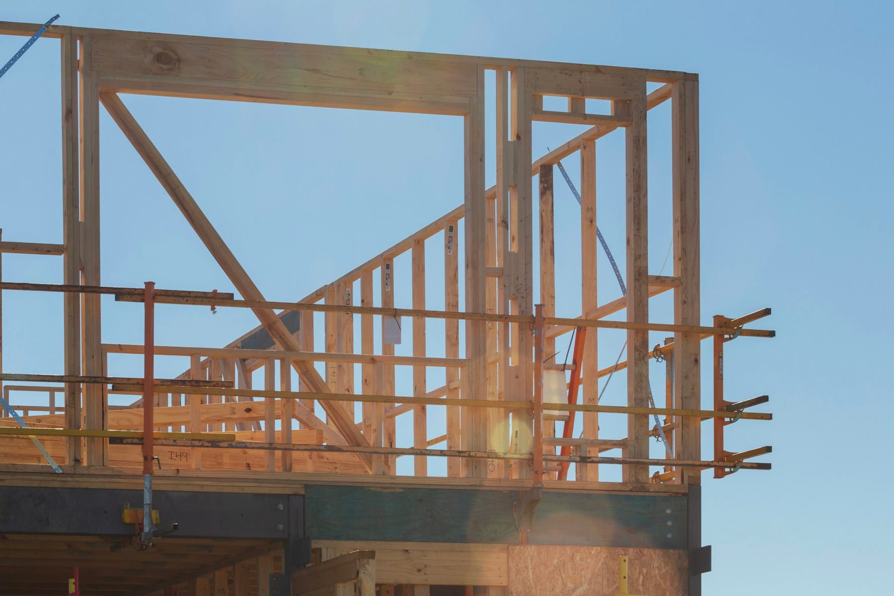 Wood framing of a new building rising against a clear blue sky
