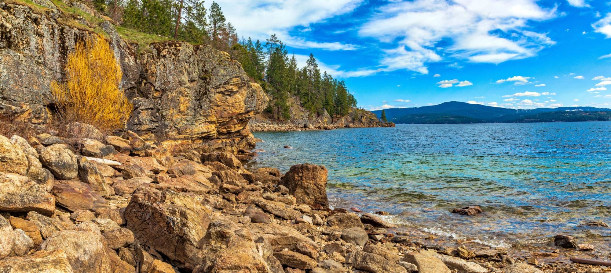 Rocky shoreline and blue water of Lake Coeur d'Alene near Coeur d'Alene, Idaho