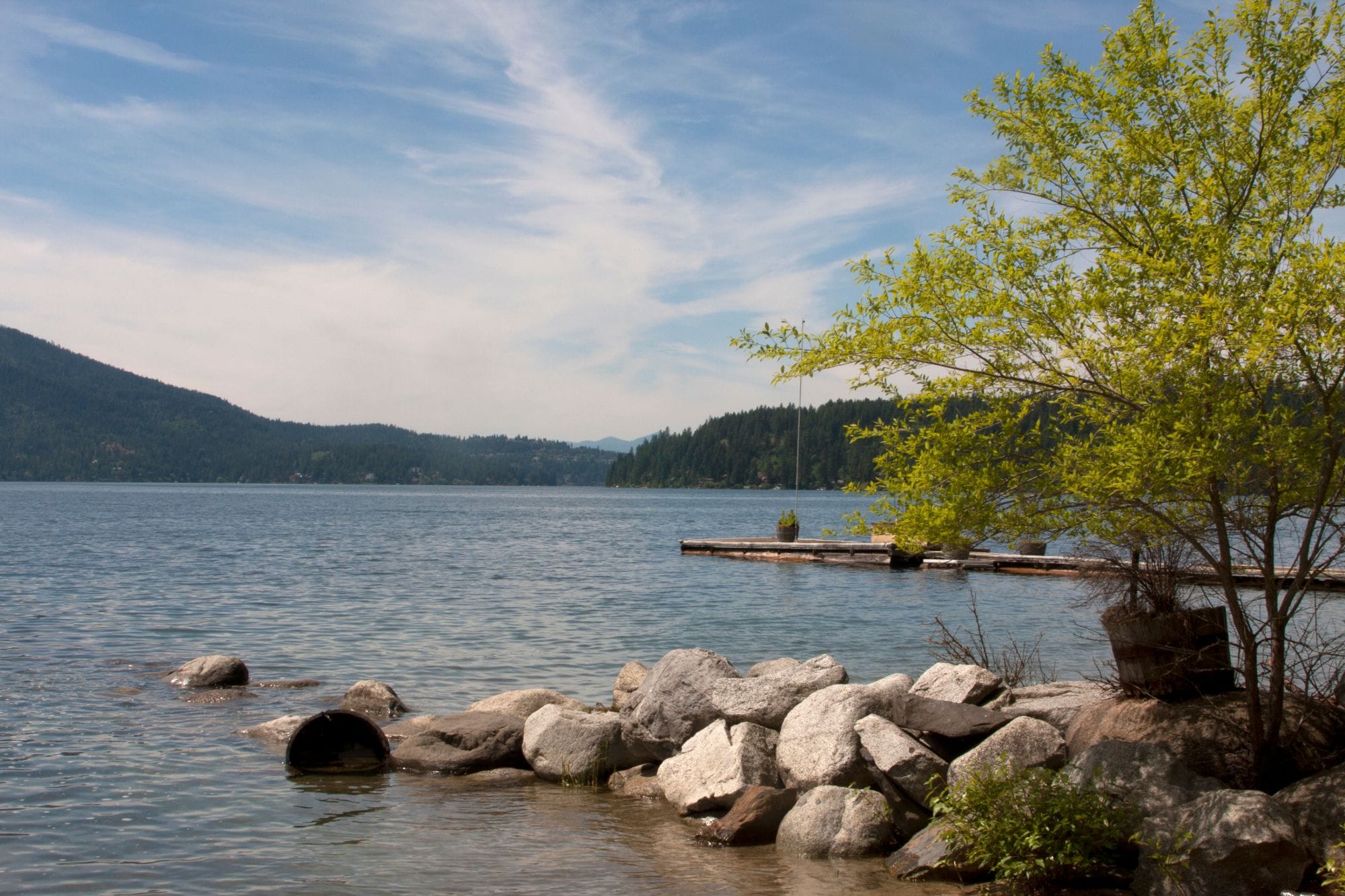 Calm lake shoreline with boulders, a dock, and forested hills near Hayden, Idaho