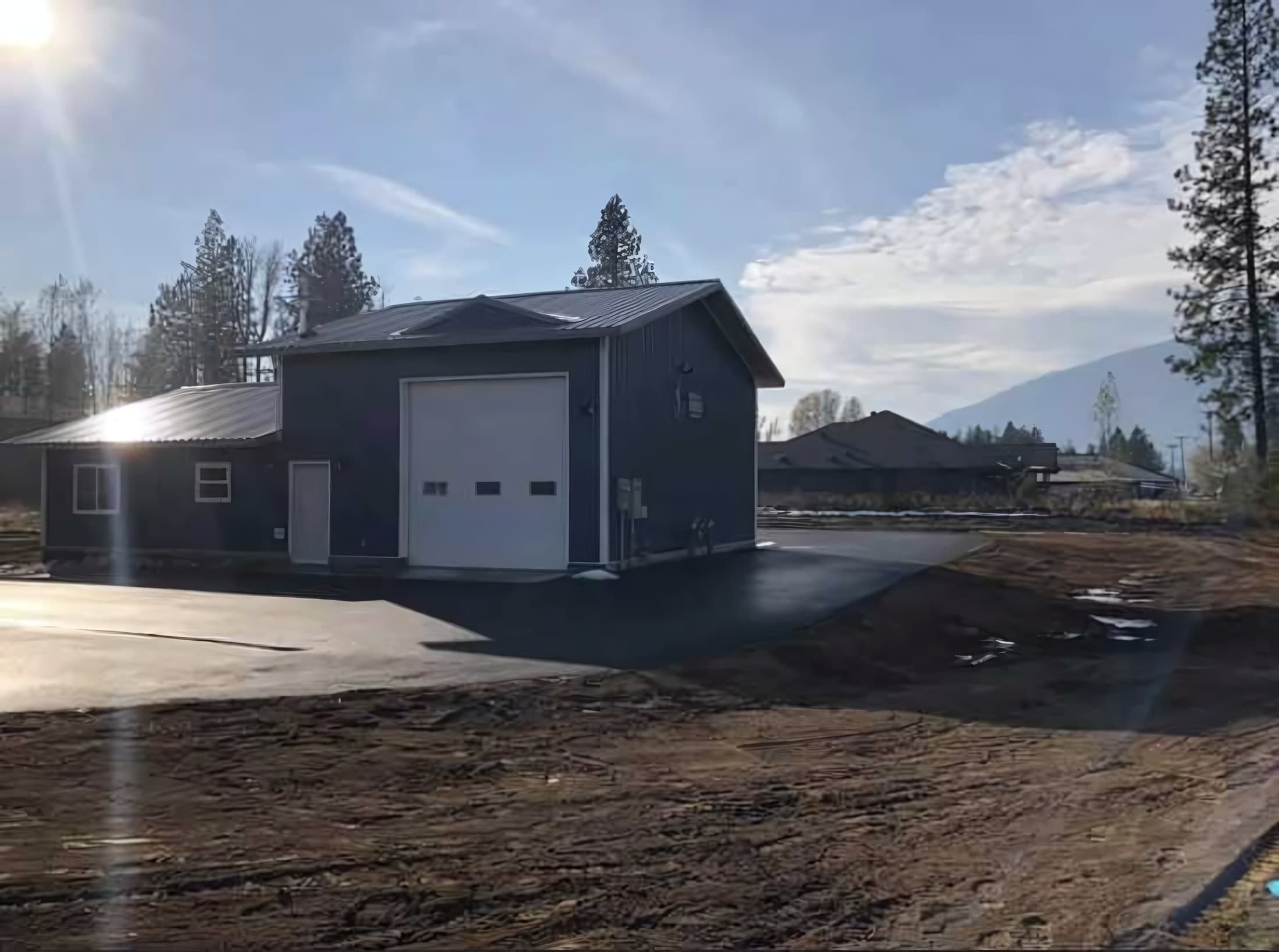 Side view of the Bonner County EMS satellite facility with a white bay door, paved lot, and mountains beyond