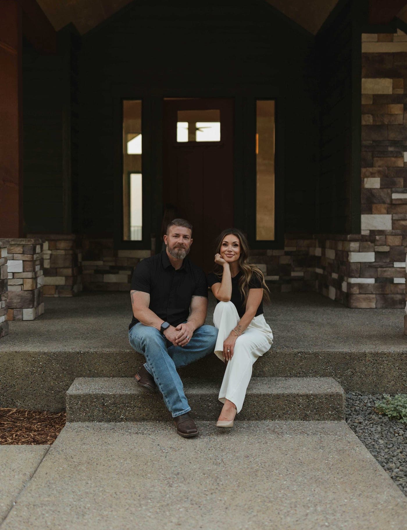 The owners of ONYX Construction sitting on the front porch steps of a home they built